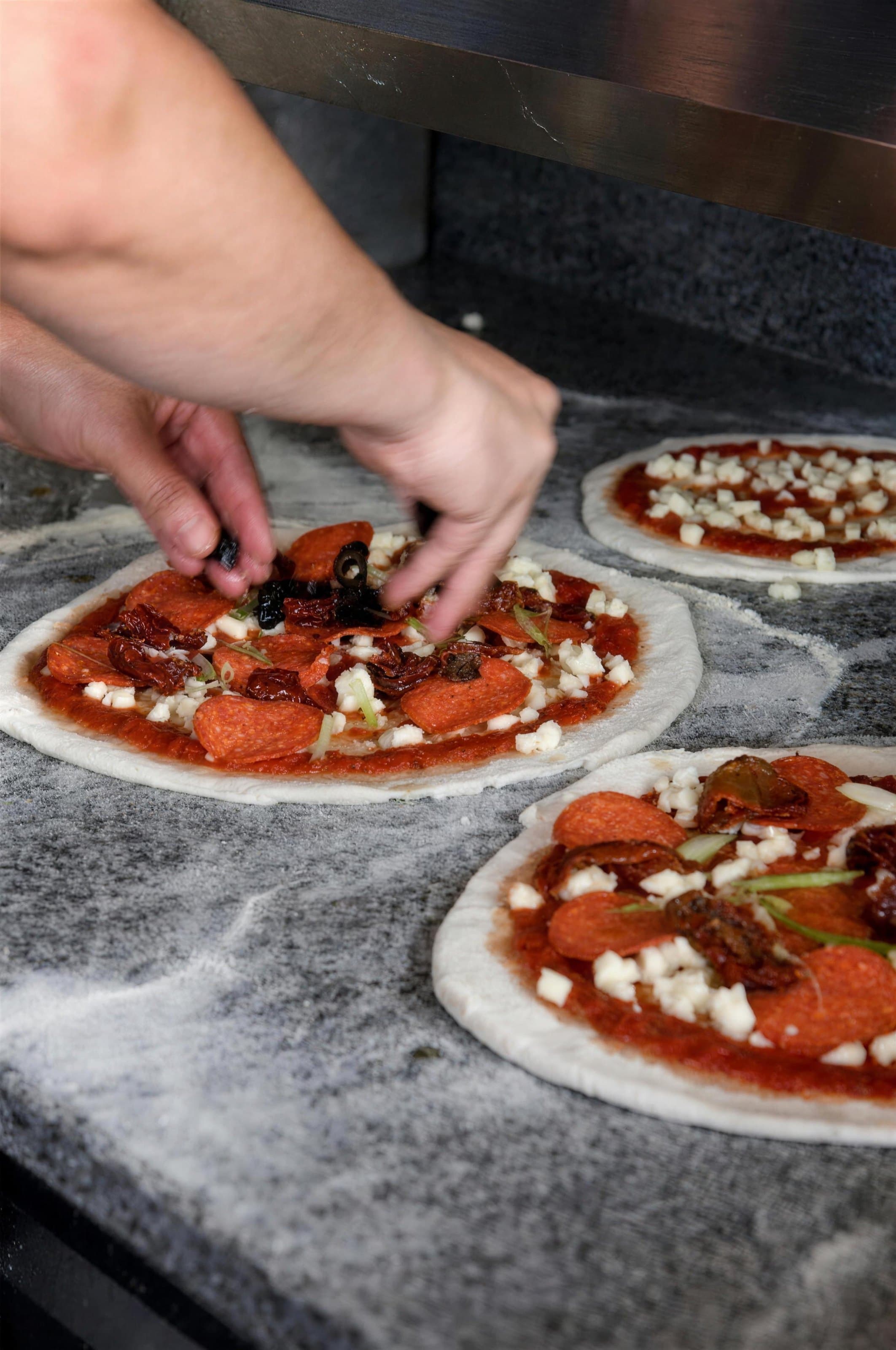 Hands topping a pizza in the kitchen