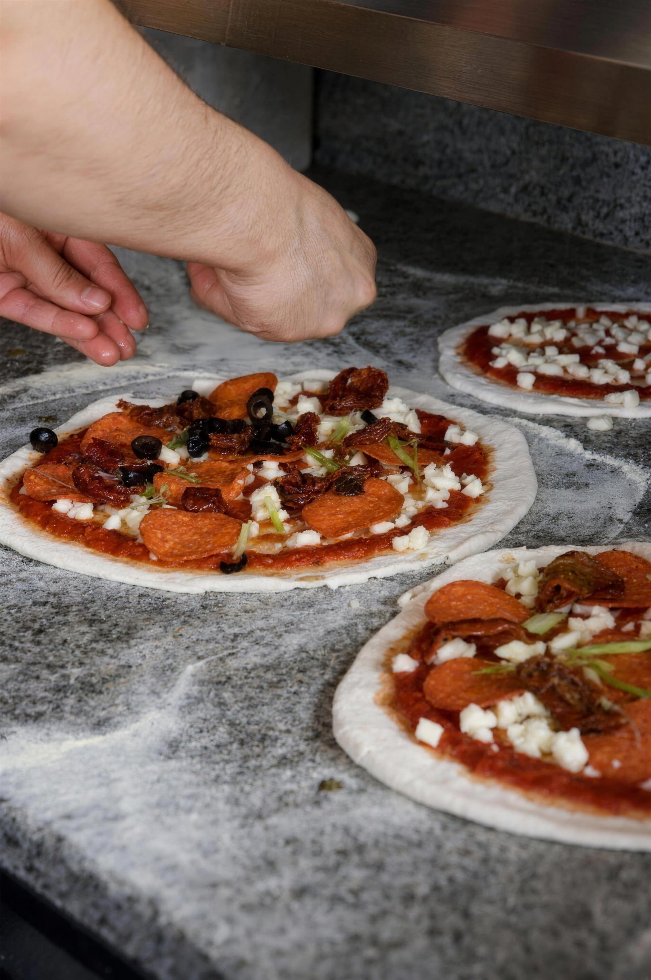 A pizza being topped by hand in the kitchen