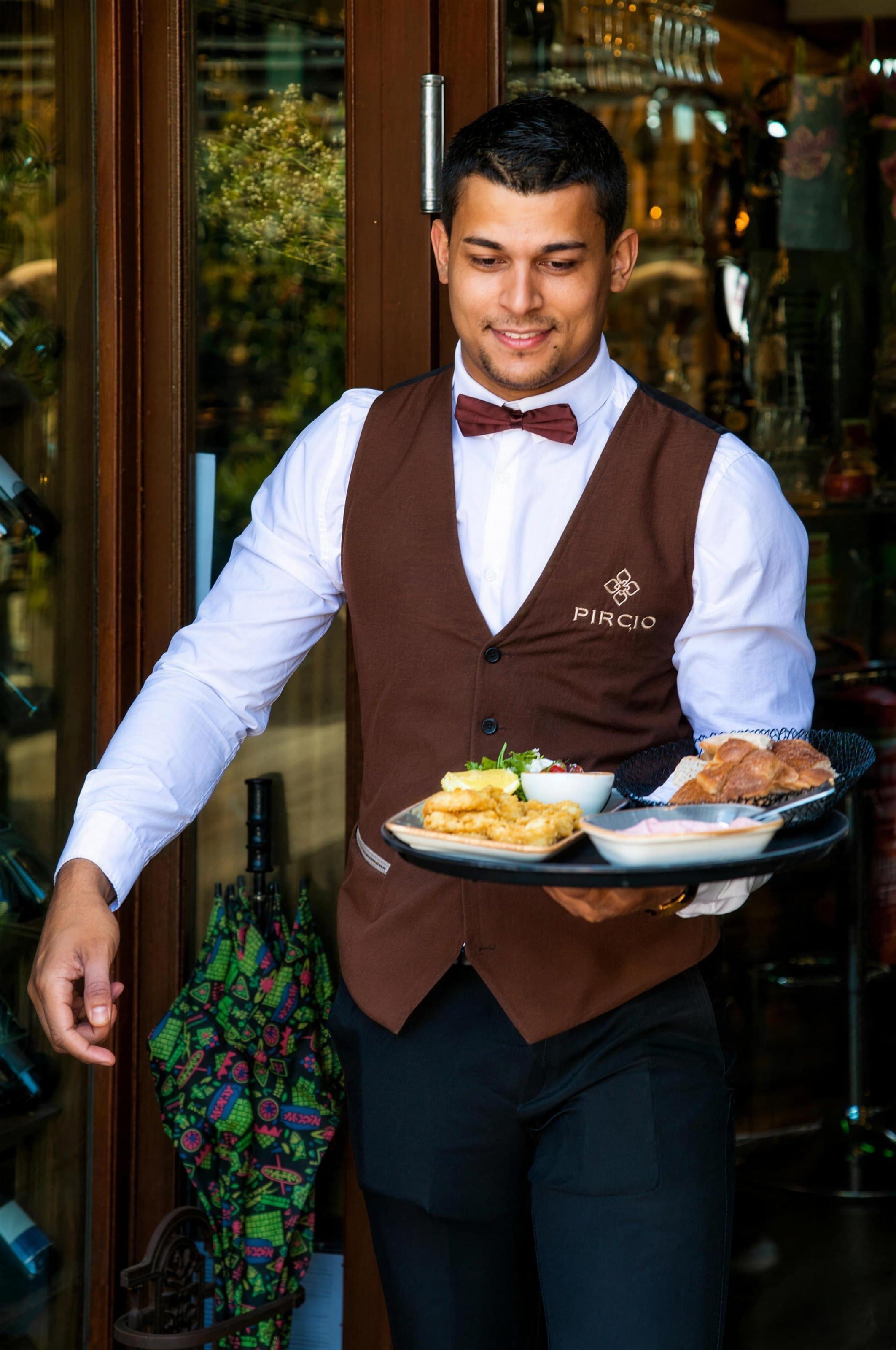 A waiter in a brown waistcoat carrying plates out to the terrace